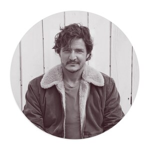 Peut inclure: Portrait en sépia d'une personne portant une veste en velours côtelé marron avec un col en peau de mouton crème. La personne a des cheveux foncés et ondulés et une moustache, sur fond de bois blanc.
