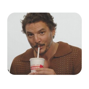 Peut inclure: Un homme aux cheveux bruns et à la barbe boit dans un gobelet blanc avec un logo rouge et blanc qui dit "Shake Shack" et "The Guys".