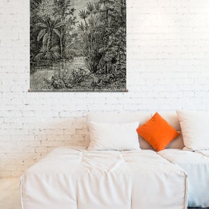 May include: A black and white illustration of a lush jungle scene with tall trees, ferns, and a small stream. The illustration is framed and hanging on a white brick wall above a white couch with orange and white pillows.