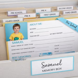 May include: A white memory box labeled "Samuel Memory Box" with file folders for school grades. A photo of a child is on a "About Me" form. The form has a blue ribbon that says "Pre School 2021-2022".
