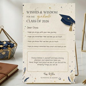 Può includere: Un biglietto di laurea con il testo "Wishes & Wisdom for the Graduate Class of 2026" e un'illustrazione di un cappello di laurea. Il biglietto include un messaggio a Olivia e auguri. Una penna e una stella dorate sono sul tavolo.
