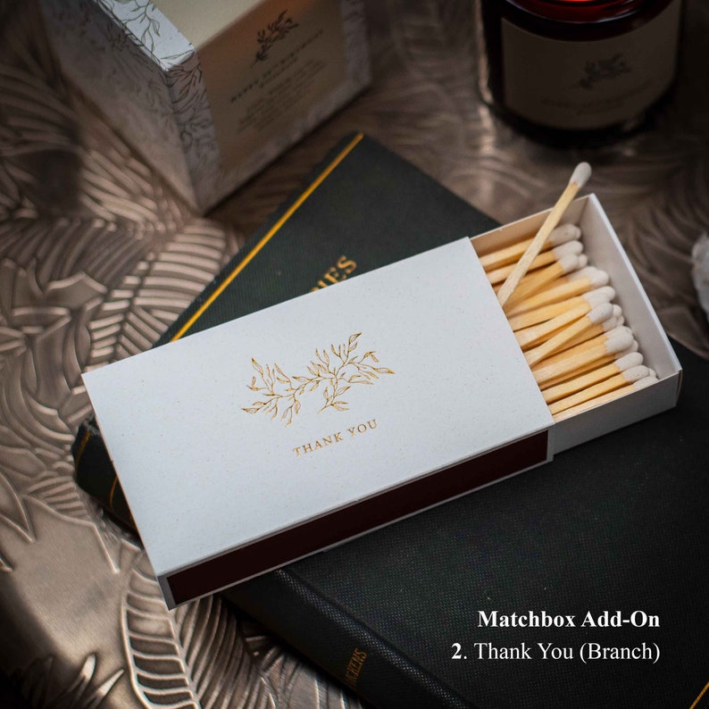 May include: White matchbox with a gold floral design and the text "Thank You". The matchbox is open and filled with wooden matches with white tips.