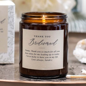 May include: A brown glass candle with a white label that says "Thank You Bridesmaid". The label also includes a personalized message: "Emma, Thank you so much for all you have done for me leading up to today. I'm so lucky to have you in my life. Love always, Sarah x"