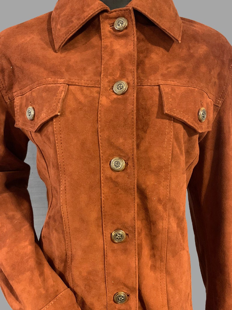 May include: A brown suede jacket with a button-up front and two flap pockets. The jacket has a classic denim-inspired style.