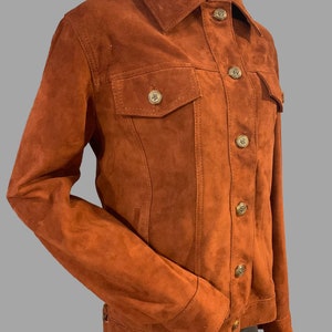 May include: A brown suede jacket with a button-up front and two flap pockets. The jacket has a classic denim style.