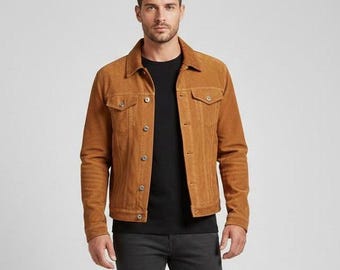 May include: A tan suede jacket with button closures and two chest pockets. The jacket is worn over a black t-shirt and paired with dark gray pants. The jacket has a classic, casual style.