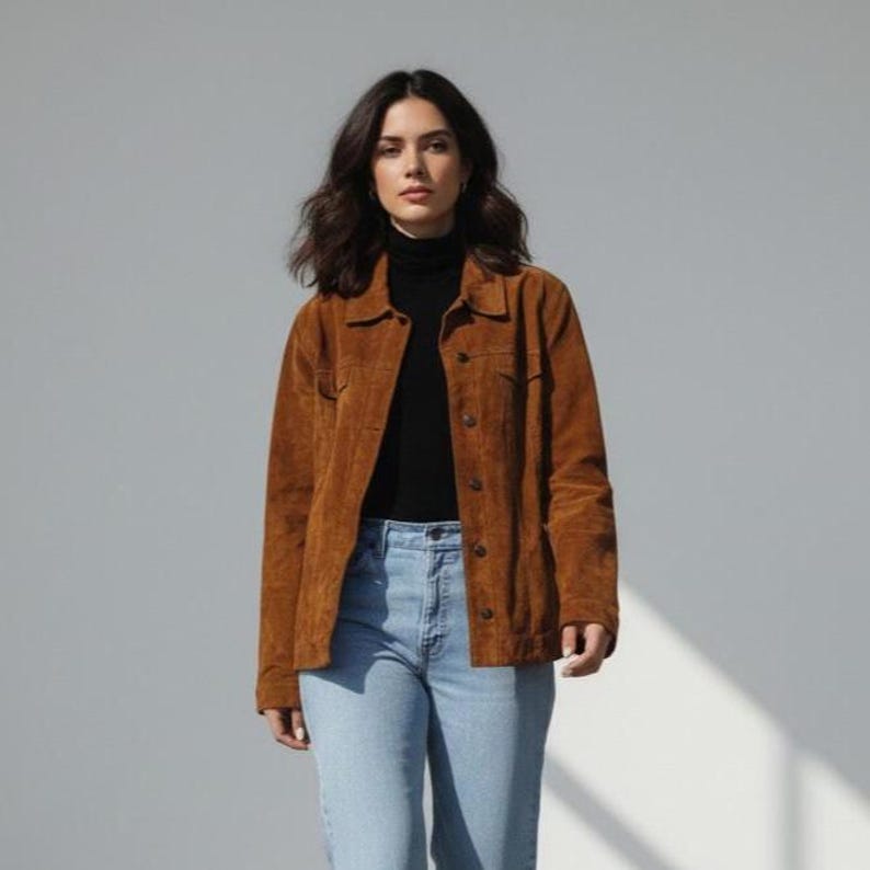 May include: A woman wearing a brown corduroy jacket over a black turtleneck and light blue jeans. The jacket has a button-up front and two chest pockets. The outfit is casual and stylish, suitable for everyday wear.