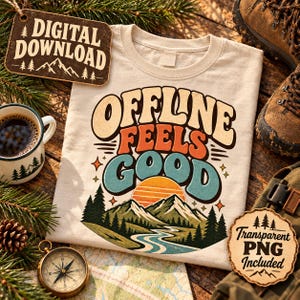 May include: A cream-coloured t-shirt featuring a graphic with the text "OFFLINE FEELS GOOD" in retro-style lettering. The design includes a sunset over a mountain range with a winding river and pine trees, accented by small four-pointed stars.