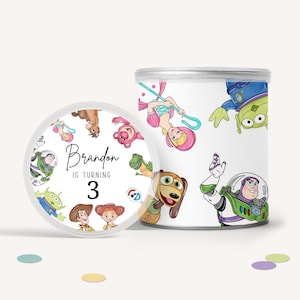 May include: White cylindrical container and lid featuring Toy Story characters. The lid has the text "Brandon is turning 3" with cartoon images. The container has images of Buzz Lightyear, aliens, and other characters.