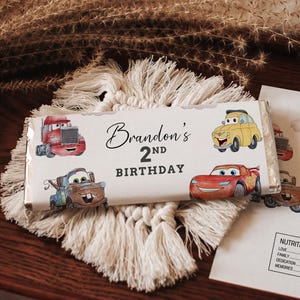 May include: A chocolate bar wrapper and a card with a Cars theme. The wrapper features illustrations of cartoon cars and the text "Brandon's 2nd Birthday". The card has the same design and includes a nutrition facts section.