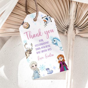 May include: A white tag with a brown string features illustrations of characters from a popular animated film. The tag includes the text "Thank you for celebrating this magical day with me! Love, Emilia."
