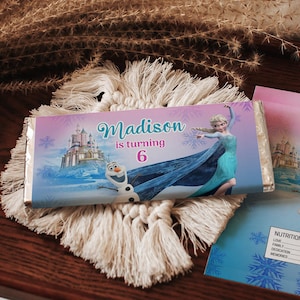 Puede incluir: Envoltorio de barra de chocolate y tarjeta con temática de Frozen. El envoltorio y la tarjeta tienen un fondo degradado rosa y azul con el texto "Madison cumple 6 años". El diseño incluye a Elsa, Olaf y un castillo.
