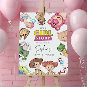May include: A wooden easel displays a baby shower sign with the text "It's a Girl Story" and "Welcome to Sophie's Baby Shower". The sign features Toy Story characters and is surrounded by pink balloons against a pink brick wall.
