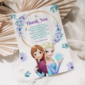 以下が含まれることがあります： 映画「アナと雪の女王」のキャラクター、アナとエルサが登場するサンキューカード。カードには「Thank You」の文字と感謝のメッセージが書かれた金の円形のフレームがあります。紫と青の花柄がテキストとキャラクターを囲んでいます。