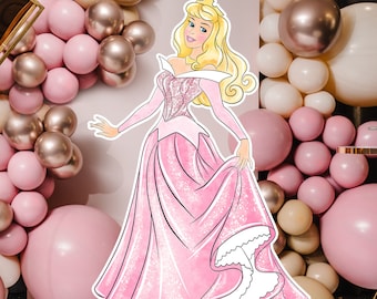 May include: A cutout of Princess Aurora in a pink gown with a glittery bodice, blonde hair, and a gold crown. The princess is surrounded by pink, gold, and white balloons, creating a festive party atmosphere.