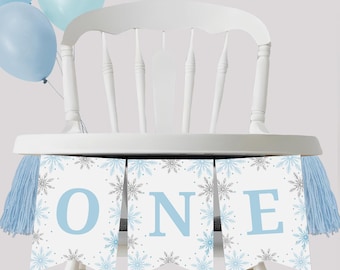 May include: A white high chair decorated with a banner that says "ONE" in light blue letters. The banner is decorated with snowflakes and has blue tassels on each end. Light blue balloons are tied to the chair.