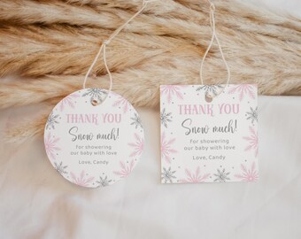 以下が含まれることがあります： 「THANK YOU Snow much!」の文字が筆記体で書かれた2つのギフトタグ。1つは丸型、もう1つは四角型。どちらもピンクとシルバーの雪の結晶のデザインで、「for showering our baby with love, Love, Candy.」の文字が入っています。