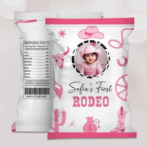 Puede incluir: Bolsa de chips rosa y blanca con una foto de una niña pequeña con un sombrero de vaquero rosa. La bolsa tiene un diseño rosa y blanco con una bota de vaquero, un cactus, un lazo, una herradura, una rueda de carro y una calavera. El texto en la bolsa dice "Sofia's First Rodeo".