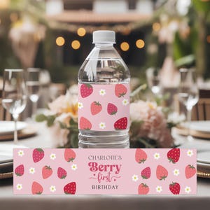 May include: Pink and white water bottle labels with a strawberry pattern and the text "Charlotte's Berry First Birthday".