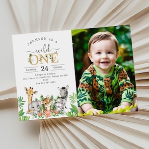 Op de afbeelding: Een jungle-thema eerste verjaardagsinvitation met een foto van een babyjongen. De uitnodiging heeft een gouden 'een' met groene bladeren en een schattige dierenillustratie. De tekst luidt 'Jackson is a wild one' en bevat de datum, tijd en locatie van het feest.