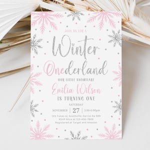 May include: A pink and silver invitation for a Winter Onederland party. The invitation features a snowflake design and the text "Join us for a Winter Onederland, Our Little Snowflake, Emilia Wilson is turning one, Saturday, November 27, 3:00-6:00pm, 123, Tunas st, Southville, Harrys Da 589, RSVP Alice at 123-456-7889, Registered at Target and Amazon."