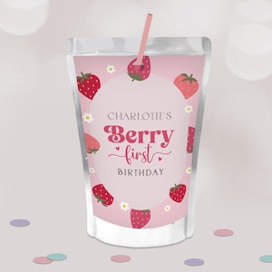 May include: A pink juice pouch with a strawberry design. The text "Charlotte's Berry First Birthday" is displayed in a circular design. Strawberries and white flowers decorate the pouch, and a pink straw is inserted.