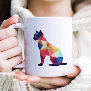 May include: White ceramic mug with a colorful geometric design of a cat sitting on the side.