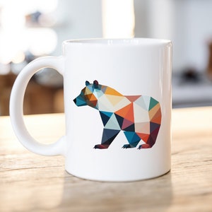 May include: White ceramic mug with a geometric design of a bear in shades of blue, orange, yellow, and red.