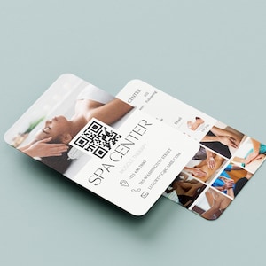 May include: A white business card with the text "SPA CENTER" in black lettering. The card also includes a phone number, address, email address, and a QR code. The back of the card features a collage of photos showing different types of massage therapy.