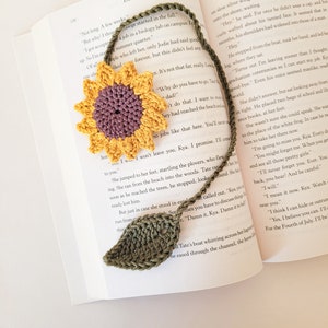 May include: A crocheted sunflower bookmark with a purple centre and yellow petals. The bookmark is attached to a green crocheted leaf.
