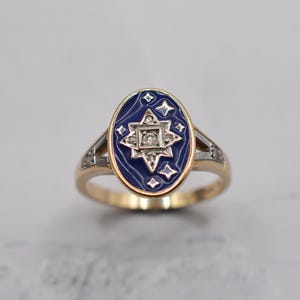 Peut inclure: Bague en or avec un centre ovale bleu foncé orné d'un motif en étoile blanche avec de petits diamants. La bague a un anneau délicat avec des accents de diamants supplémentaires, créant une esthétique vintage.