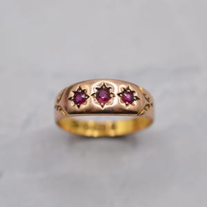 以下が含まれることがあります： 3つの赤い宝石が星型のデザインにセットされたゴールドリング。リングは丸みを帯びたバンドで、ヴィンテージまたはアンティークの可能性があります。宝石は深い赤色で、金は温かみのある光沢のある仕上がりです。