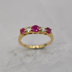 Może przedstawiać: Biały ceramiczny kubek z czarnym uchwytem i napisem "But First, Coffee" pogrubioną, czarną czcionką. Kubek jest wypełniony ciemnym płynem, prawdopodobnie kawą, i stoi na jasnej powierzchni.