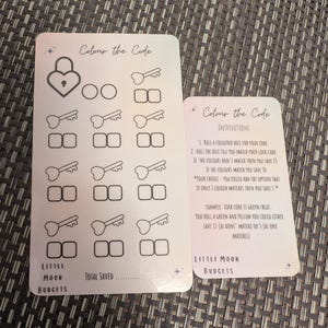 May include: Two white cards with the text "Colour the Code" and illustrations of keys, locks, and boxes. One card has instructions. The cards are designed for budgeting and saving money. The brand name "Little Moon Budgets" is visible.