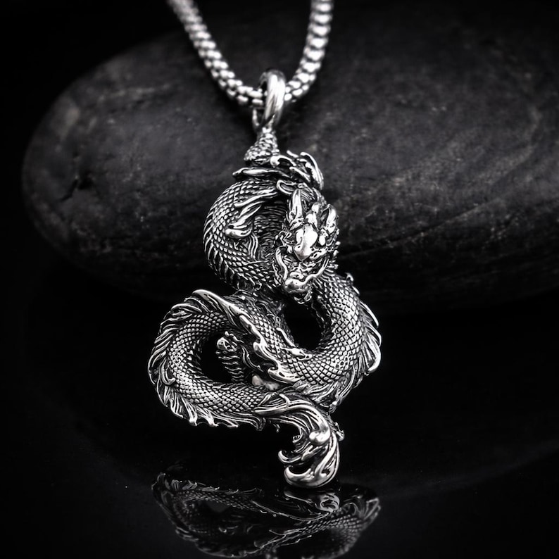 May include: A silver dragon pendant necklace. The pendant features a detailed dragon design with scales, claws, and a fierce expression. The dragon is coiled around itself, and the necklace has a chain.