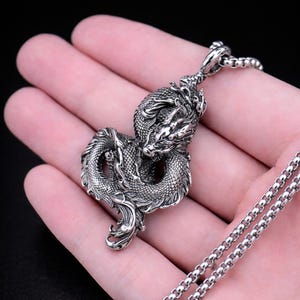 May include: A detailed silver dragon pendant on a matching chain. The dragon is intricately sculpted with scales and a fierce expression. The chain is a classic box link style, creating a bold accessory.