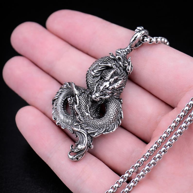May include: A detailed silver dragon pendant on a matching chain. The dragon is intricately sculpted with scales and a fierce expression. The chain is a classic box link style, creating a bold accessory.