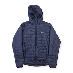 May include: A dark navy blue hooded jacket featuring a quilted square pattern throughout the exterior. The jacket includes a full-length front zip, two zipped side pockets, and a small Patagonia brand logo patch on the upper left chest.