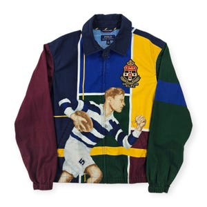 May include: A color-blocked zip-up jacket featuring a dark blue collar, a maroon left sleeve, and a green right sleeve. The front displays a large graphic of a rugby player in a blue and white striped shirt, with a crest patch reading Polo Ralph Lauren.