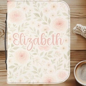 May include: A floral-patterned case with the name "Elizabeth" in pink script. The case features a cream background with pink roses and green leaves. A black handle is visible on the left side. The case is likely for a tablet or notebook.