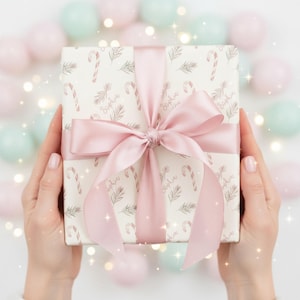 May include: A wrapped gift with a pink bow and ribbon. The gift wrap is white with a pattern of candy canes, sprigs, and the name "Sophia". The background has pastel-colored spheres and bokeh.