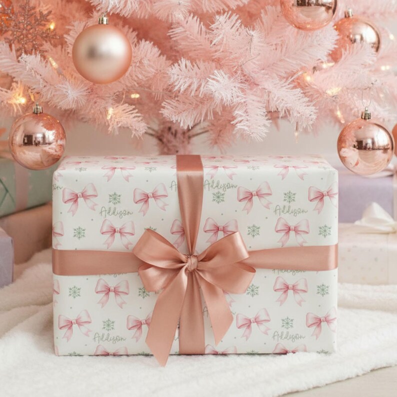 A neatly wrapped gift with a pink bow sits under a pastel pink Christmas tree with matching ornaments.