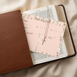 May include: A brown leather Bible with a matching cover, open to reveal a Bible study notes card and a silver cross necklace. The notes card has a floral border and the words "Bible Study Notes".
