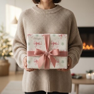 A person wearing a beige knit sweater holds a gift wrapped in patterned paper with a pink ribbon.