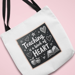 Puede incluir: Bolso tote blanco con asas negras. Presenta un diseño gráfico de pizarra con el texto "Teaching is a Work of HEART", corazones, estrellas, manzanas y un libro abierto. Un regalo ideal para profesores.