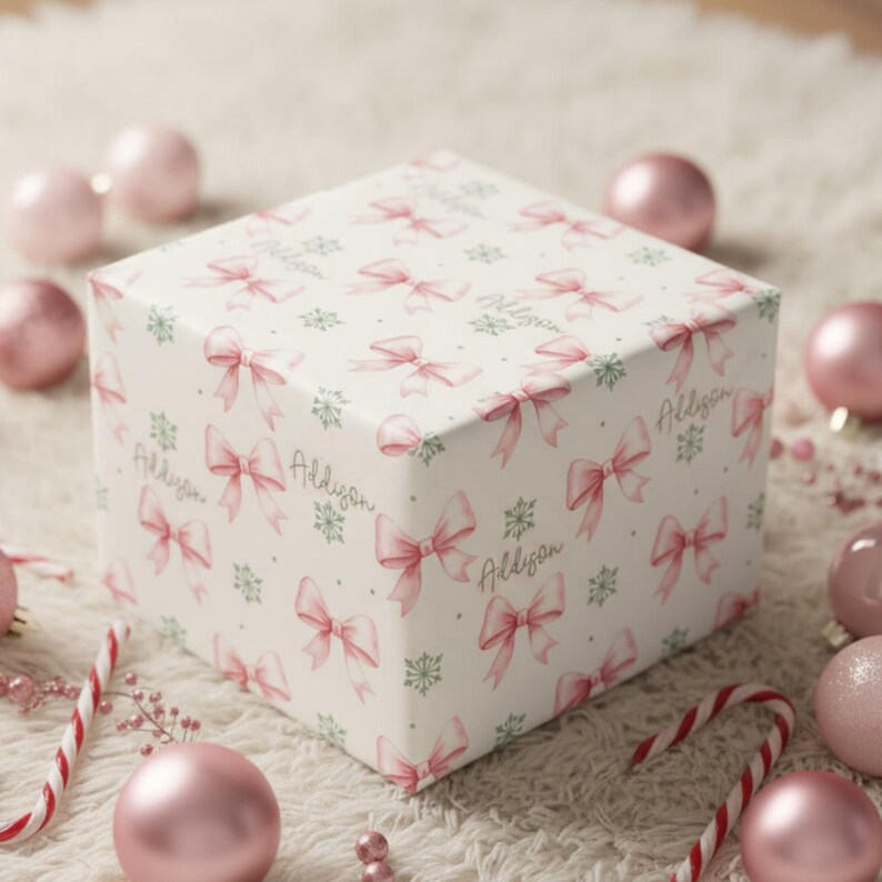 A gift box wrapped in pink bow paper is surrounded by Christmas ornaments and candy canes on a fuzzy white rug.