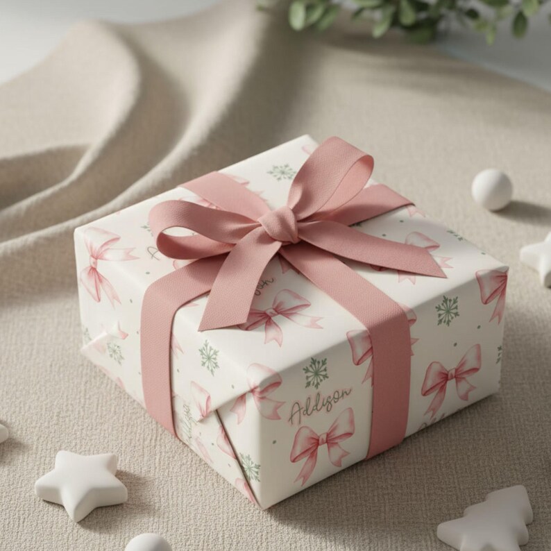 A neatly wrapped package with a pink bow sits on a textured fabric surface near star-shaped decorations.