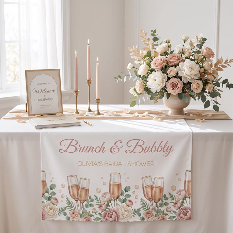 Pu&ograve; includere: Allestimento tavola per un addio al nubilato con tovaglia bianca e runner con la scritta "Brunch & Bubbly" e illustrazioni di calici di champagne. La scena comprende una composizione floreale, candele e un cartello di benvenuto, creando un'atmosfera elegante.