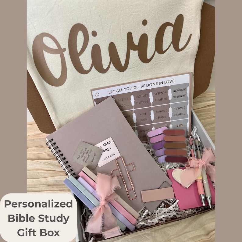 May include: A personalized Bible study gift box with the name "Olivia" printed on the lid. The box contains a notebook, pens, bookmarks, and a cross-shaped paper clip. The text "Personalized Bible Study Gift Box" is visible.