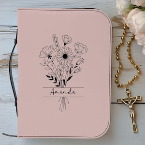 以下が含まれることがあります： ピンクのフェイクレザーのジャーナルで、花柄のデザインと「Amanda」という名前が前面に印刷されています。ジャーナルには黒いストラップ留めがあります。